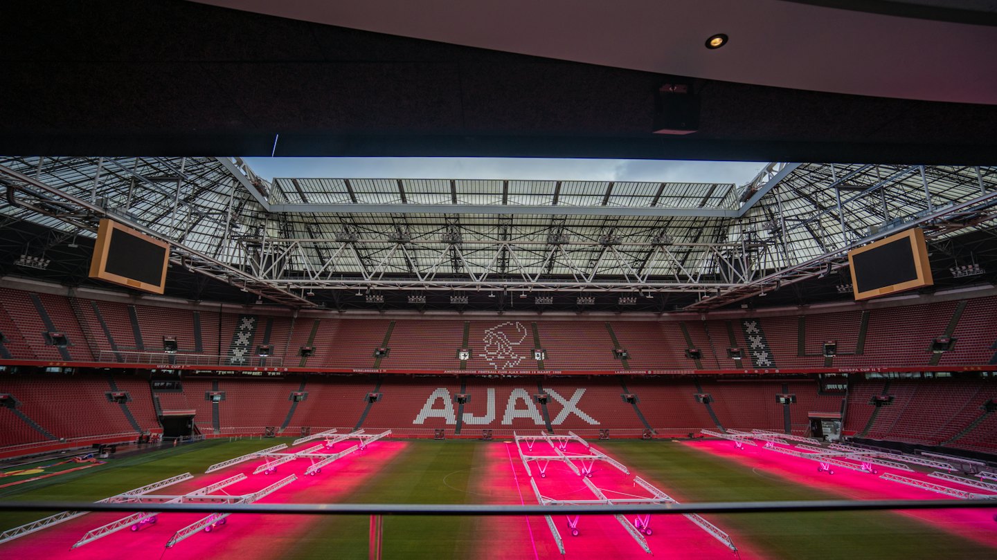 Empty modern sports stadium with red seating and grass pitch.